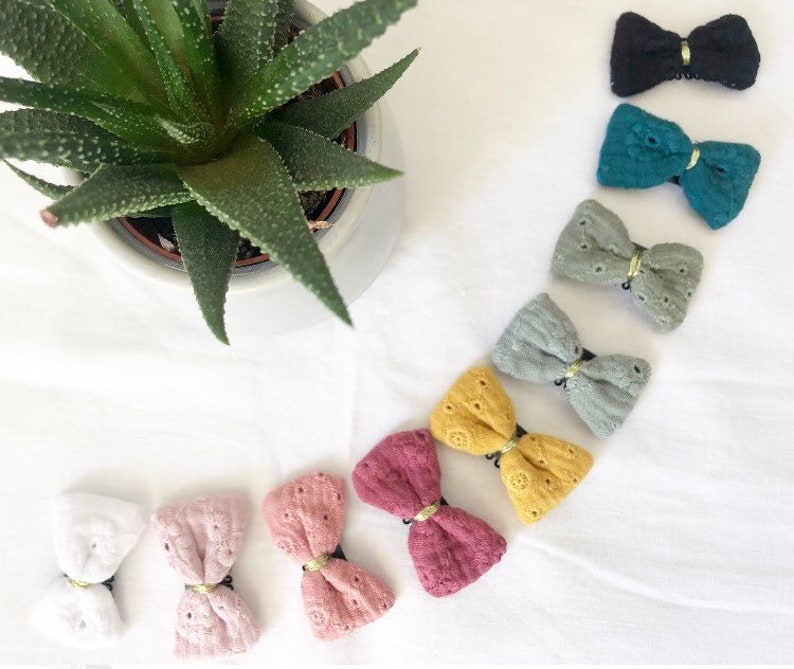 May include: Assortment of ten fabric hair bows in various colors, including white, pink, red, yellow, green, and black. Each bow has a gold accent in the center.