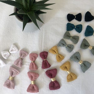 May include: Assortment of handmade fabric hair bows in various colors and patterns, including white, pink, green, and yellow. The bows are made with a delicate lace fabric and feature gold accents.