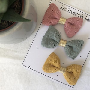 May include: Three fabric hair bows with gold trim. The bows are pink, green, and yellow. The bows are displayed on a white card with the text "Les Tr&eacute;sors de Java".
