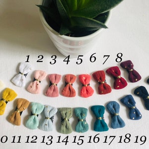 May include: Twenty small fabric hair bows with gold accents and white polka dots in various colors, including white, pink, red, brown, blue, and green. The bows are numbered 1 through 20.