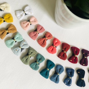 May include: A collection of 15 fabric hair bows with gold glitter accents. The bows are in various colors, including yellow, pink, blue, green, and red.