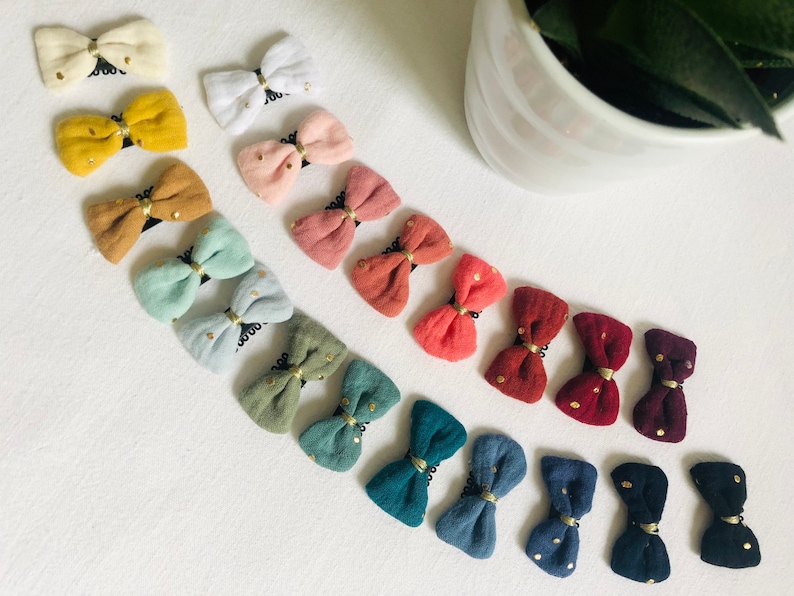May include: A collection of 15 fabric hair bows with gold glitter accents. The bows are in various colors, including yellow, pink, blue, green, and red.