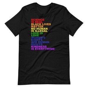 May include: Black t-shirt with a rainbow-colored message that reads "Science is real, Black Lives Matter, No Human is Illegal, Love is Love, Women's Rights are Human Rights, Kindness is Everything."