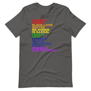 May include: A dark gray t-shirt with a rainbow-colored message that reads "Science is Real, Black Lives Matter, No Human is Illegal, Love is Love, Women's Rights are Human Rights, Kindness is Everything."