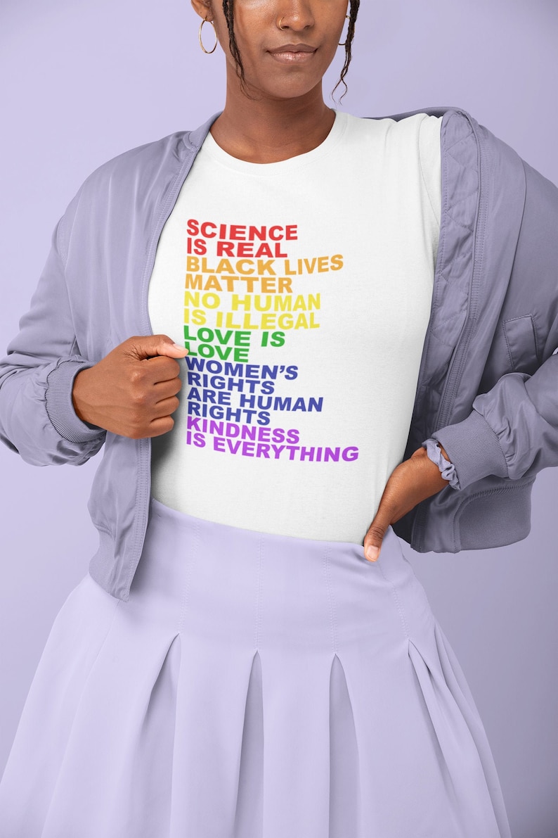 May include: A white t-shirt with a rainbow-colored message that reads "Science is real, Black Lives Matter, No human is illegal, Love is love, Women's rights are human rights, Kindness is everything."