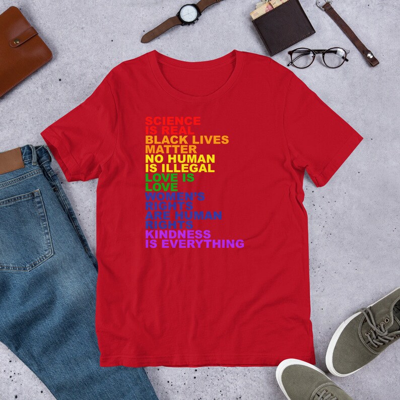 May include: Red t-shirt with a rainbow-colored message that reads "Science is real, Black Lives Matter, No Human is Illegal, Love is Love, Women's Rights are Human Rights, Kindness is Everything."