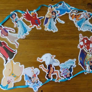 Op de afbeelding: Een blauwe lintenslinger met uitsparingen van personages uit de Disney-film Aladdin. De personages zijn Aladdin, Jasmine, Abu, Jafar, de Genie en Rajah.