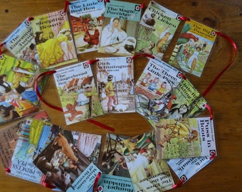Puede incluir: Una guirnalda de 14 portadas de libros coloridas que representan cuentos clásicos para niños como "La Gallinita Roja", "La Bella Durmiente", "El Hombre de Jengibre" y "Los Tres Cerditos". Las portadas están unidas a una cinta roja y tienen un círculo rojo con un número blanco en cada una.