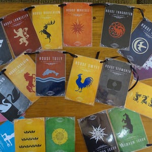 Puede incluir: Un conjunto de 14 tarjetas coloridas con una cuerda negra unida a cada tarjeta. Cada tarjeta presenta un escudo de armas diferente de la casa de la popular serie de televisión Game of Thrones. Las tarjetas están impresas con el nombre de la casa y un símbolo.
