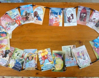 May include: A garland of illustrated book covers featuring various Shakespearean plays, including "Macbeth," "Hamlet," and "Romeo and Juliet." Each cover is rectangular, with a black ribbon attached for hanging. The covers are arranged in an oval shape on a wooden surface.