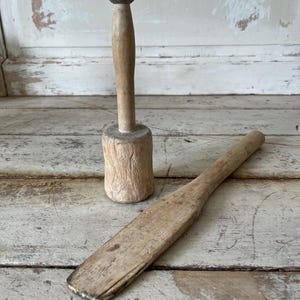 May include: Two wooden kitchen utensils: a wooden mallet with a rounded head and a wooden spatula. The utensils are on a whitewashed wooden surface.