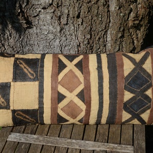 May include: A long, rectangular pillow with a brown, black, and beige geometric pattern. The pillow is made of a woven fabric and has a fringed edge.