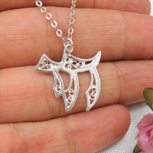 May include: A silver filigree pendant necklace featuring the Hebrew letter Chai, a symbol of life. The pendant is delicate and intricate, with a delicate chain.