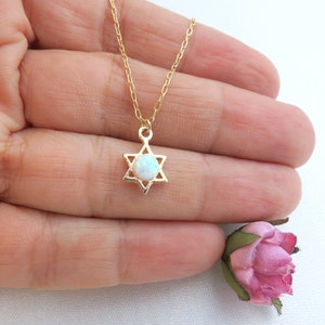 Puede incluir: Collar de cadena dorada con un pequeño colgante de Estrella de David con una piedra de ópalo blanca.