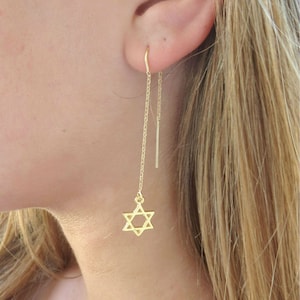 May include: Gold dangle earrings with a star of David charm on one side and a thin gold bar on the other side.