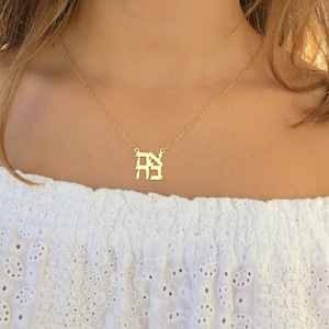 May include: A gold necklace with a delicate chain and a pendant featuring two initials in a stylized font.
