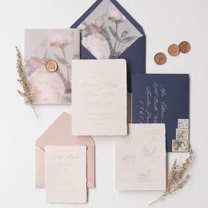 May include: Wedding invitation suite with a floral design on the envelope and a map on the RSVP card. The invitation is printed on textured paper with a delicate floral pattern. The envelope is a deep blue color and the RSVP card is a light pink color.