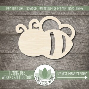 May include: Unfinished wooden cutout of a flying bee, 1/8 inch thick birch plywood. The bee is in flight with its wings spread out. The bee has a black and white striped body and a small head with two antennae. The cutout is ready for DIY painting or staining.