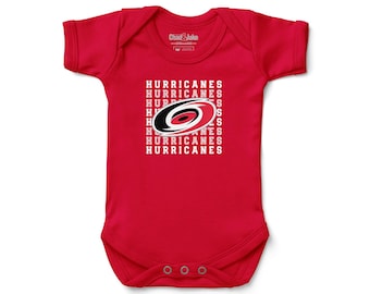 May include: Red baby bodysuit with the text "HURRICANES" in white, surrounding a logo with a black, white, and red circular design. The bodysuit has short sleeves and three snaps at the bottom.