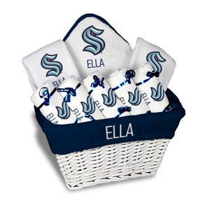 May include: A white wicker basket filled with white towels and washcloths, all featuring a blue and teal logo and the name "ELLA". The basket has a navy blue trim and is filled with rolled and folded towels.