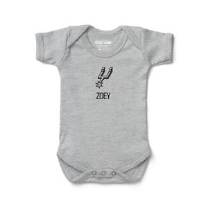 May include: A gray baby bodysuit with short sleeves. The bodysuit features a black graphic of a spur and star, with the name "ZOEY" printed below. The brand "Chad & Jake" is printed on the neckline.