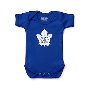 May include: A royal blue baby bodysuit with short sleeves. The front features a white Toronto Maple Leafs logo, a stylized maple leaf with the team name. The bodysuit has three snap closures at the bottom.
