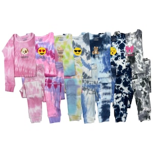 May include: Seven pairs of tie-dye pajamas for kids, each with a different emoji and name. The pajamas are in various colors, including pink, blue, green, and gray.