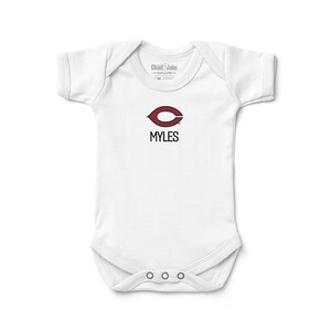 May include: White baby onesie with a maroon and white logo that says "MYLES". The onesie has short sleeves and a snap closure at the bottom. The brand name "Chad & Jake" is printed at the top.