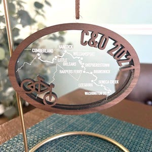 May include: A wooden ornament shaped like a bicycle wheel with a map of the C&O Canal Towpath, a popular bike route, and the text "C&O 2021".