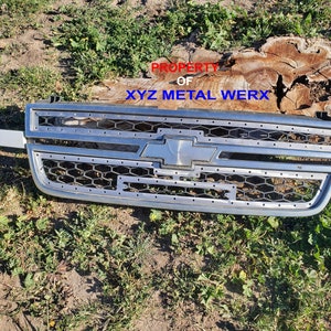 May include: A silver Chevrolet grille with a honeycomb pattern and a chrome Chevrolet logo. The grille has a black border and is labelled "PROPERTY OF XYZ METAL WERX".