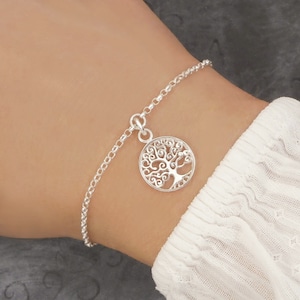 May include: A silver chain bracelet with a tree of life charm. The charm is a circle with a detailed tree design.