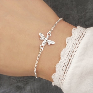 May include: A silver chain bracelet featuring a small bee charm. The bee is detailed with wings and a body.