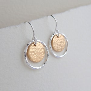 May include: A pair of silver hoop earrings with a gold hammered disc charm hanging from each hoop.