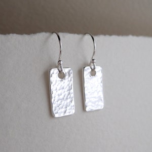 May include: A pair of silver earrings with a hammered rectangular design. Each earring has a small hole in the centre of the rectangle.