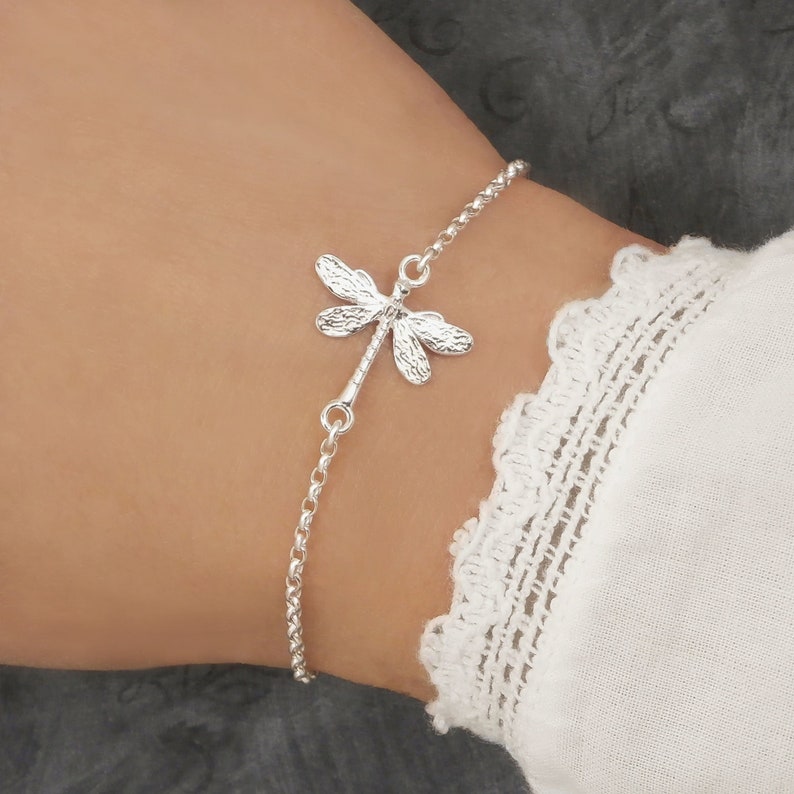 Sterling silver dragonfly bracelet for women with a dainty, detailed nature-inspired dragonfly charm on a delicate adjustable chain. Worn on a woman's wrist with a boho style sleeve for scale.