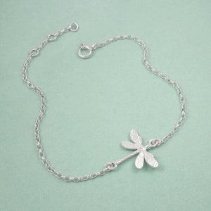 May include: A silver chain bracelet with a delicate dragonfly charm. The chain is made of small, linked circles.
