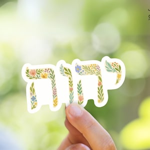 May include: A floral design sticker with the Hebrew word "Chai" which means "life" in English. The sticker is white with a light yellow background and features a variety of colorful flowers and leaves.