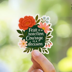 May include: A floral sticker with a green background and the text "Fear is a reaction Courage is a decision". The flowers are pink, red, and white.