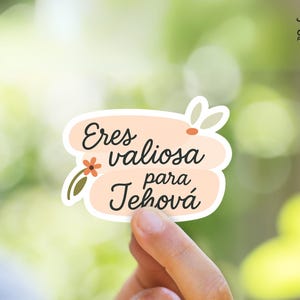Puede incluir: Una pegatina con el texto "Eres valiosa para Jehová" en escritura negra sobre un fondo color melocotón. La pegatina tiene un borde blanco y está decorada con pequeños acentos florales y de hojas. El logotipo de JW Printables está en la esquina superior derecha.