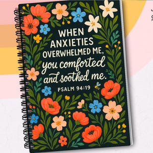 May include: A spiral-bound notebook with a black cover featuring floral illustrations in orange, pink, blue, and white. The text reads "WHEN ANXIETIES OVERWHELMED ME, you comforted and soothed me. PSALM 94:19."