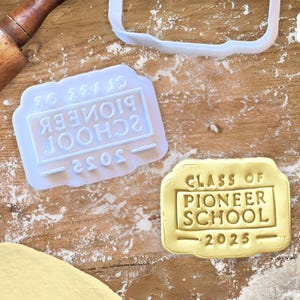 May include: A close-up of a cookie cutter and a cookie with the text "Class of 2025 Pioneer School" on it.