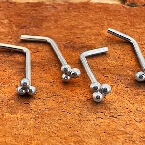 May include: Five silver nose rings with a cluster of three small balls on the end of each ring.