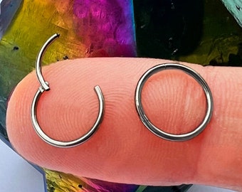 May include: Two silver hoop earrings, one slightly larger than the other, are shown on a finger against a background of a colourful iridescent crystal.
