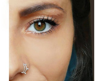 May include: Close-up of a person's face with a silver nose ring. The person has green eyes and dark hair.