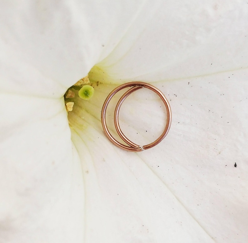 Puede incluir: Dos pendientes de aro de oro rosa, uno ligeramente m&aacute;s grande que el otro, est&aacute;n sobre un p&eacute;talo de flor blanco.
