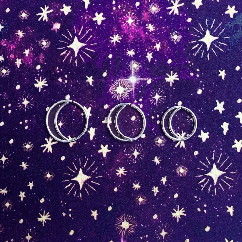 Puede incluir: Tres aros de plata sobre un fondo morado con un patr&oacute;n de estrellas blancas.
