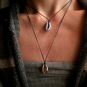 Può includere: Due collane con ciondoli a forma di conchiglia. La collana superiore ha un ciondolo a conchiglia argentato e la collana inferiore ha un ciondolo a conchiglia dorato.