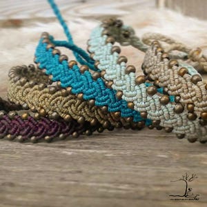 May include: Five braided bracelets with brown beads. The bracelets are in shades of teal, light green, brown, and purple.