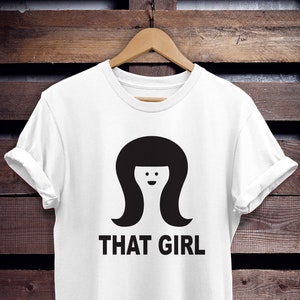 May include: White t-shirt with a black graphic of a woman with a bob haircut and the text "THAT GIRL".