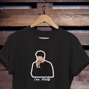 May include: Black t-shirt with a white outline of a cartoon character holding a glass of wine. The text "I'M FINE" is printed below the character.